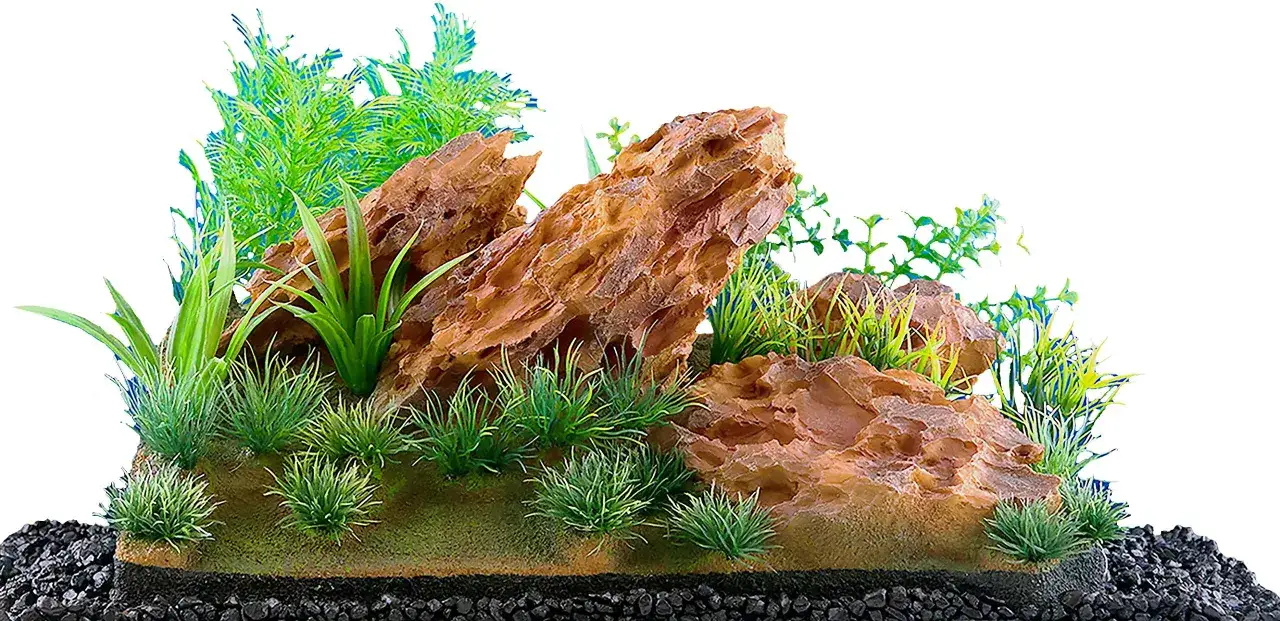 Ett inrett akvarium med bruna klippformationer, gröna konstgjorda växter och svart grus.